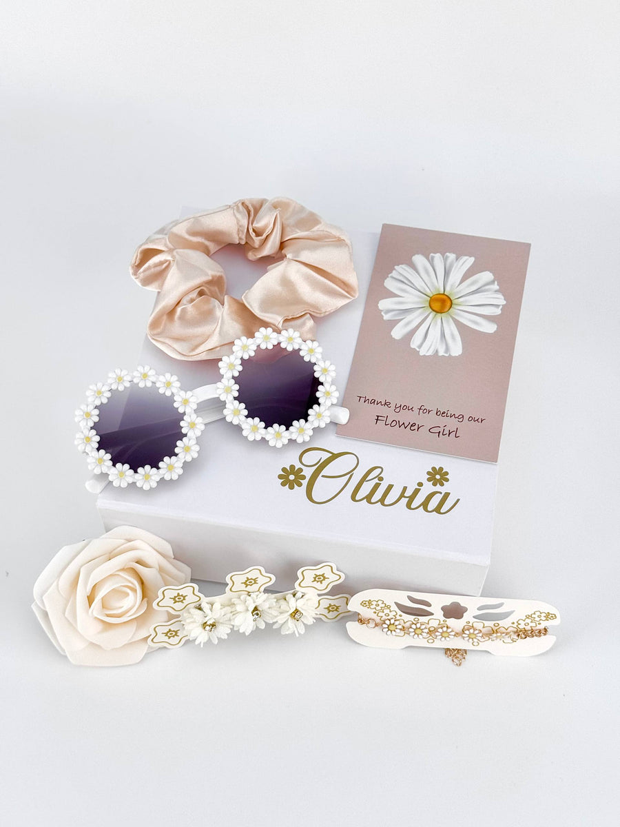 white box with gold premium vinyl personalizing the box with the flower girls name and flowers. set includes: daisy sunglasses, two bracelets, foam rose, scrunchie and a personalized card saying "thank you for being our flower girl"