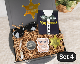 A gift box set for ring security featuring a black card reading 'Will you be our Ring Bearer?', black sunglasses, a round pin that says 'RING BEARER', a cartoon bear sticker, a gold sheriff star badge, and a agent earpiece arranged in brown paper shred inside an open black box.