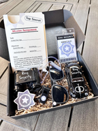 ring security proposal gift box. open box, set 1 includes a ring security "mission assignment" card with a ring security agent id badge, sunglasses, play binoculars, agent earpiece, black whistle, "ring security" sticker, personalized black car with a name. the inside of the box is filled with Kraft colored paper filler. ring bearer gift box.