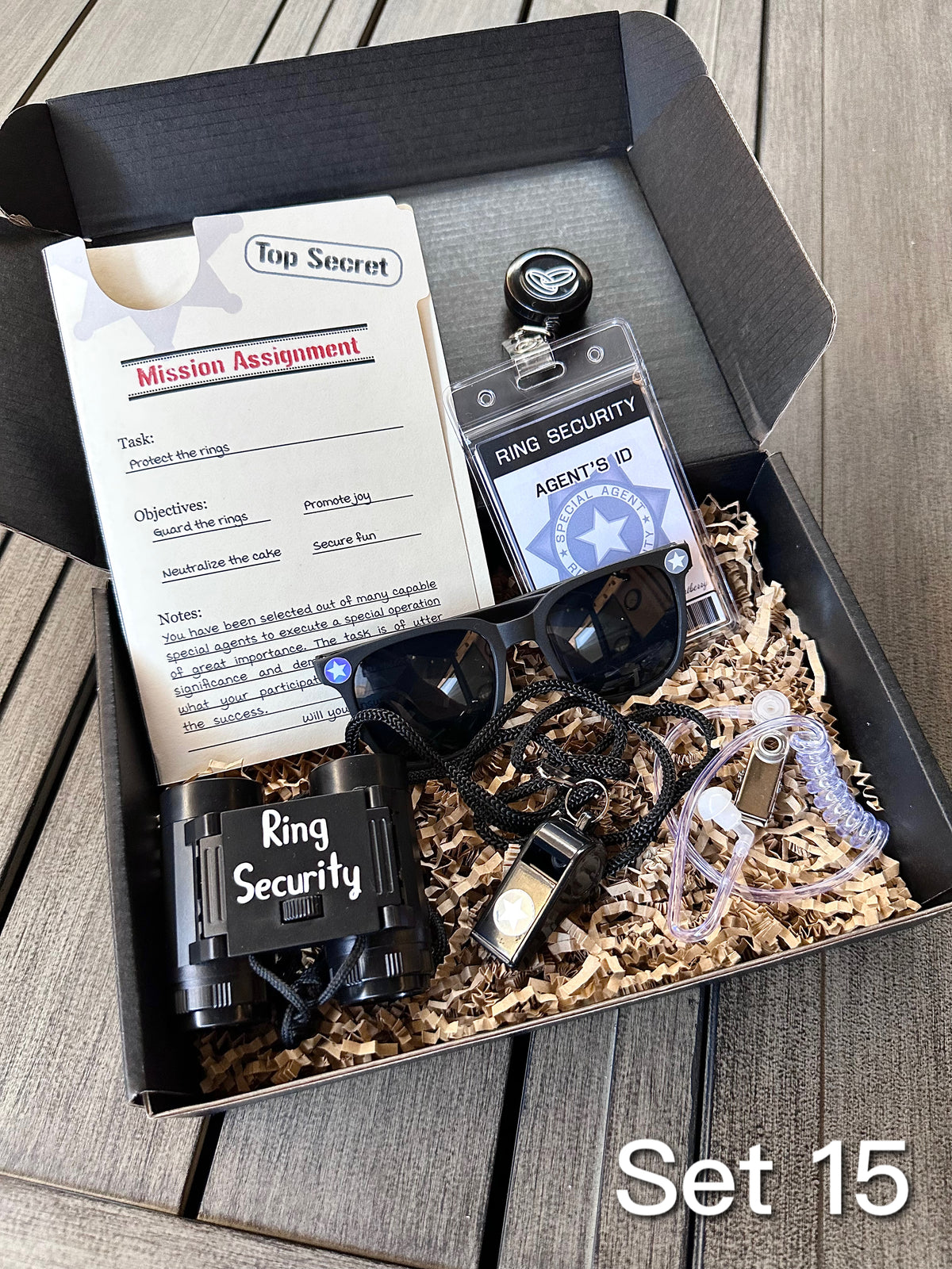 ring security proposal box. open box. set 15 includes a "mission assignment" card, an agent ID badge, sunglasses, play binoculars, agent ear piece, whistle, and brown paper filler. 